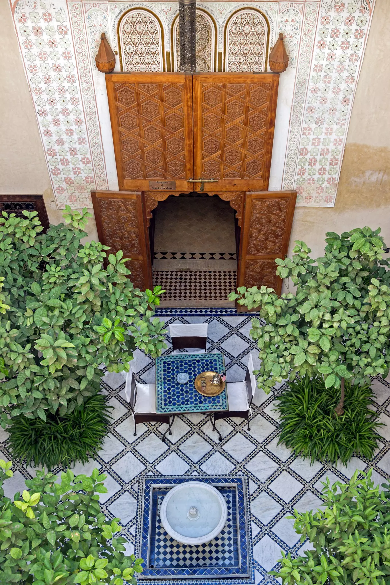 A courtyard with a tiled floor, trees and ornate wooden carved doors.