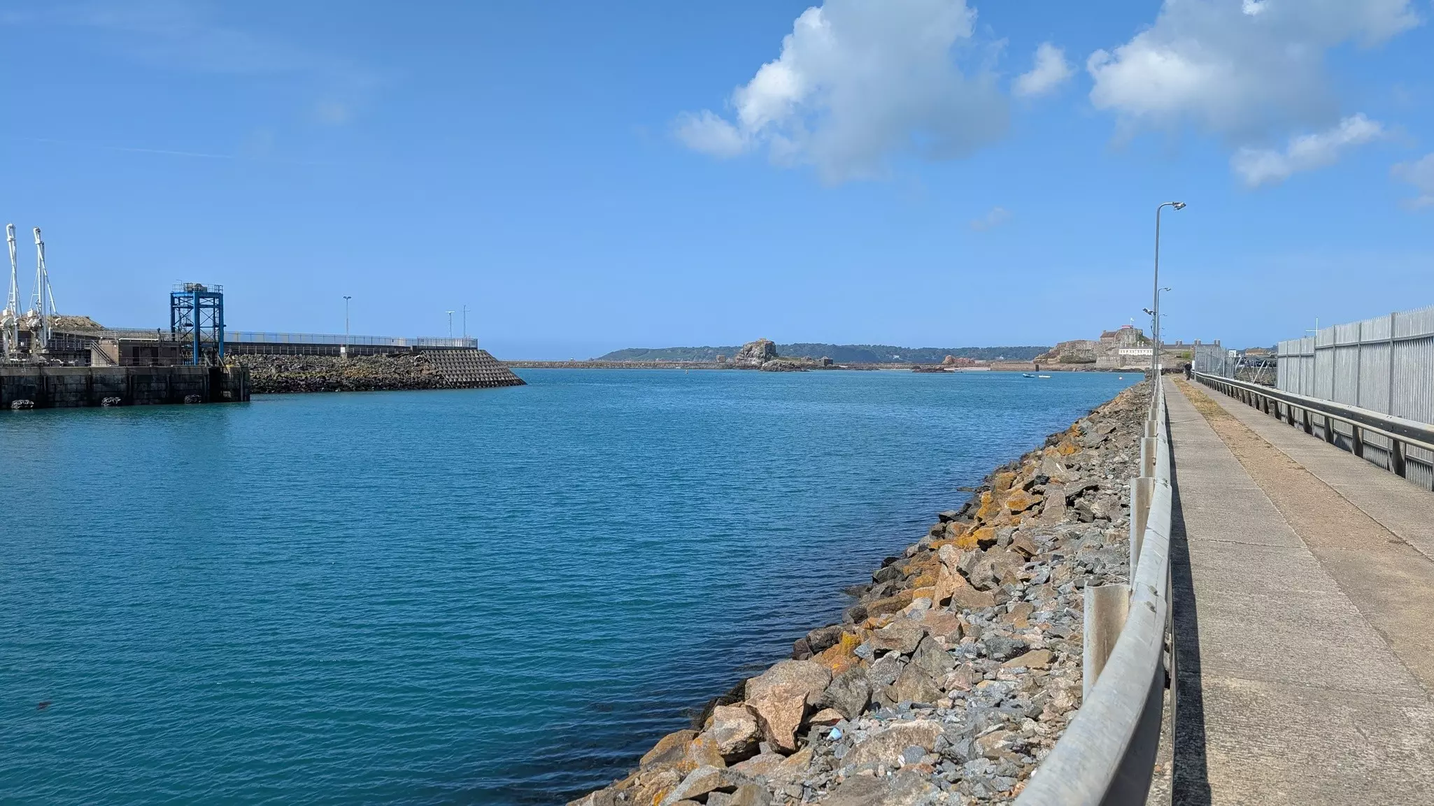 Concrete pier sided by rocks leading out into a channel with another pier to the left on a sunny day.
