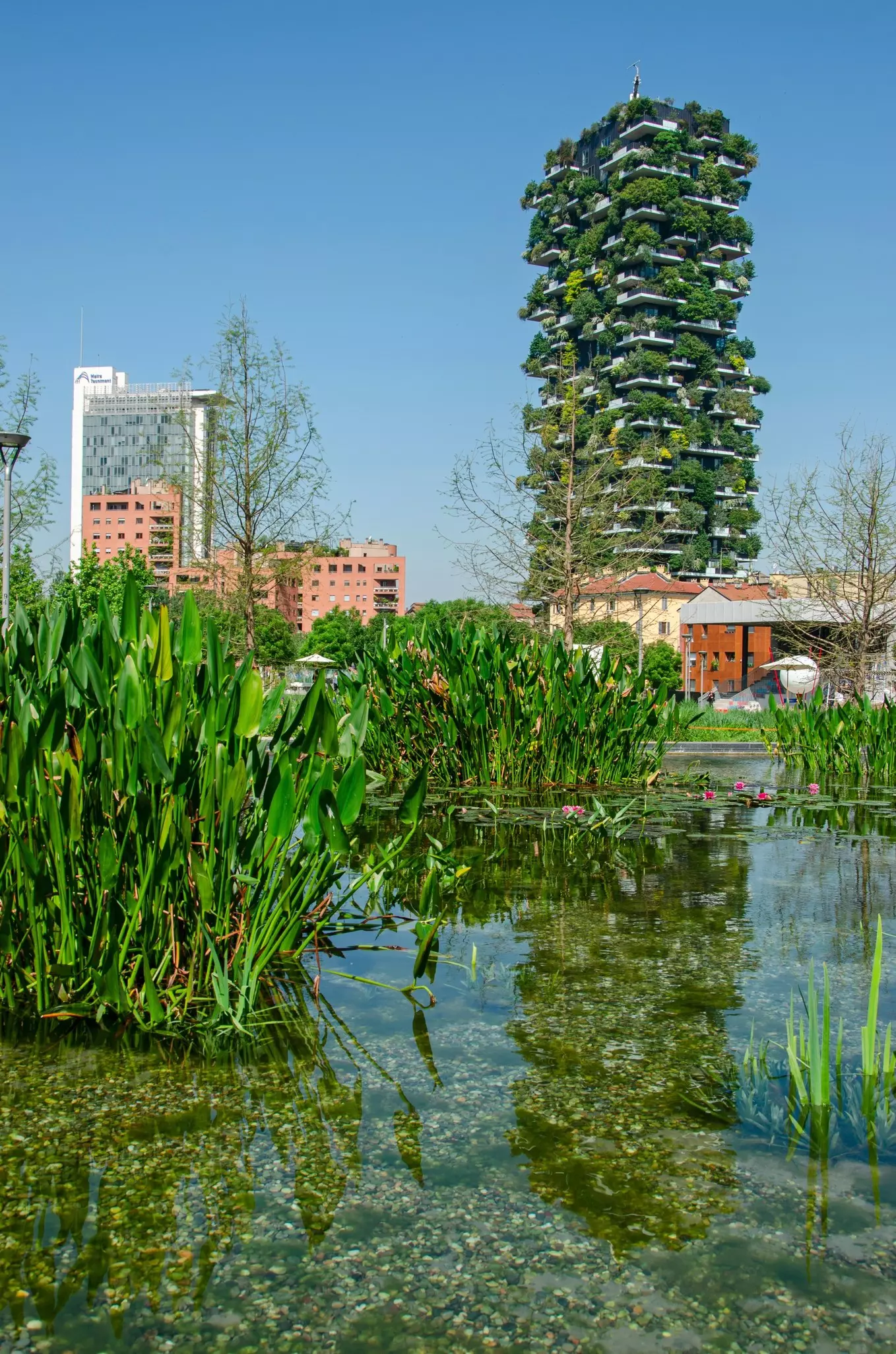 A tall residential building beside parkland with plants and trees growing among its balconies.