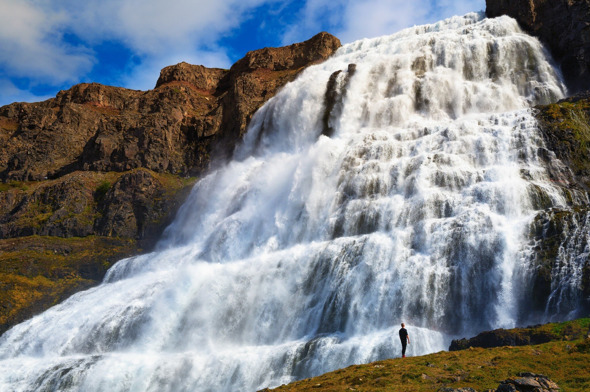 Person standing at the Dynjandi waterfall, also known as Fjallfoss, located on the Westfjords peninsula in northwestern Iceland.  License Type: media  Download Time: 2021-11-08T12:05:46.000Z  User: aniabartoszek  Is Editorial: No  purchase_order:   