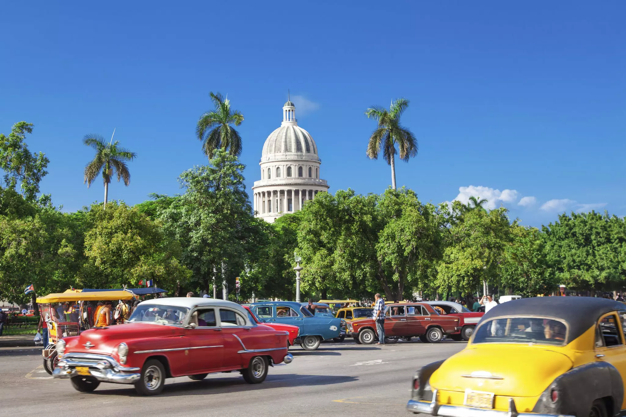 The dome of El Capitolio stands above trees and vintage cars