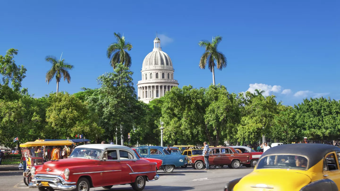 The dome of El Capitolio stands above trees and vintage cars