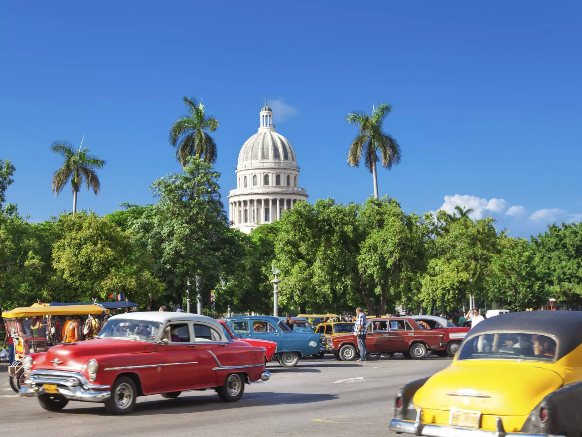 The dome of El Capitolio stands above trees and vintage cars