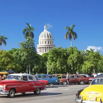 The dome of El Capitolio stands above trees and vintage cars
