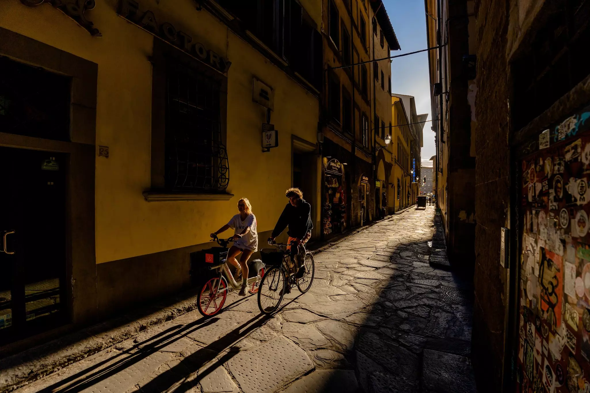Florence, Italy - May 31, 2024: Golden Hour Ride: Couple Cycling Through a Sunlit Street in Florence.