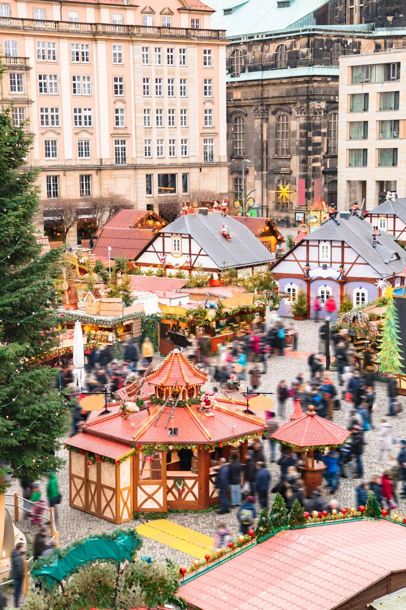 An outdoor Christmas market with different stalls, deocrations and lights, and crowds of people.