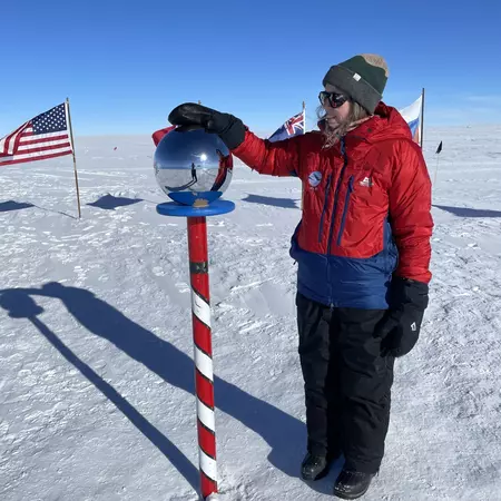 A woman places her hand on a glass orb on top of a red-and-white striped pole stuck in snow.