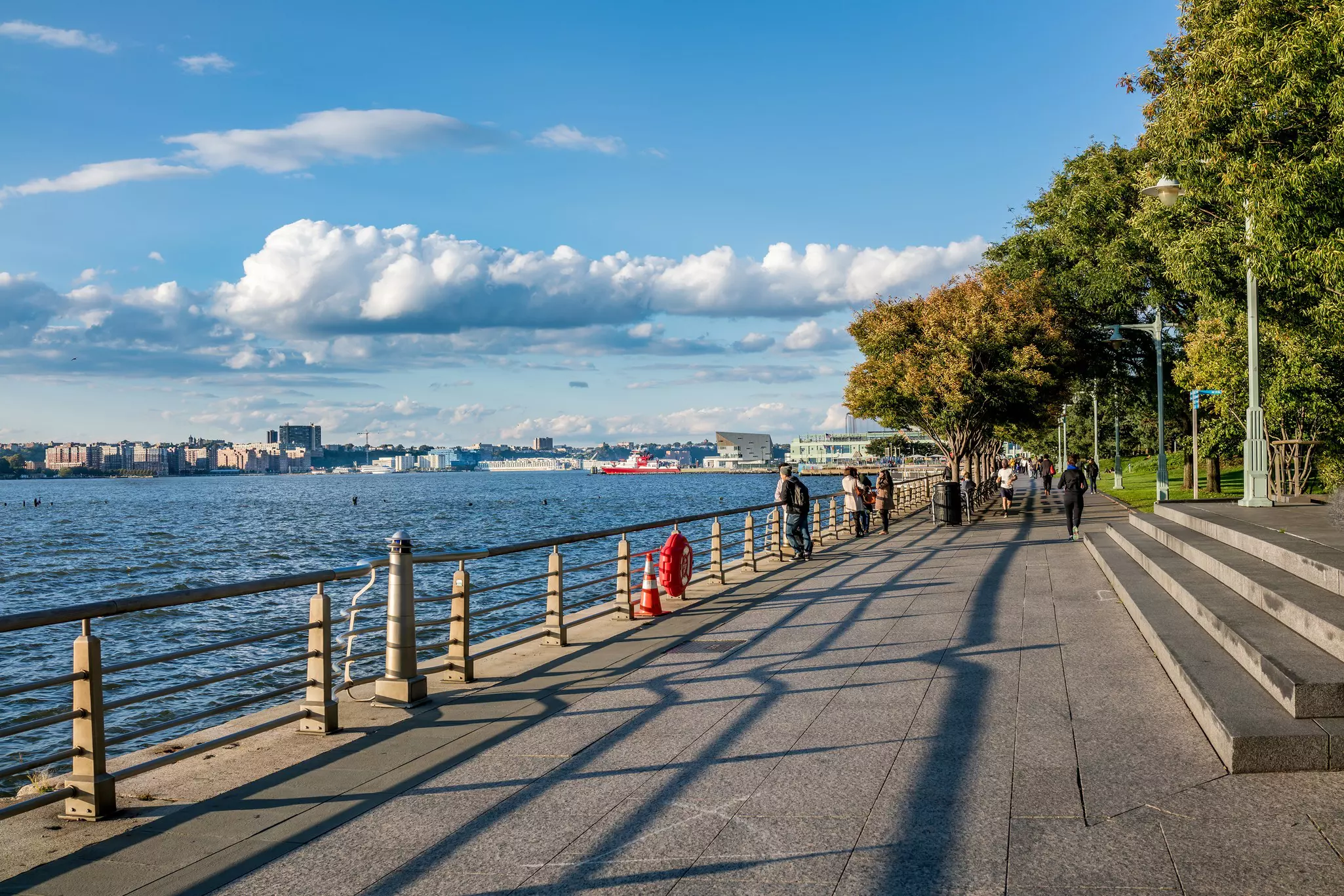 People jog and stroll along a pathwy beside a river on a sunny day.