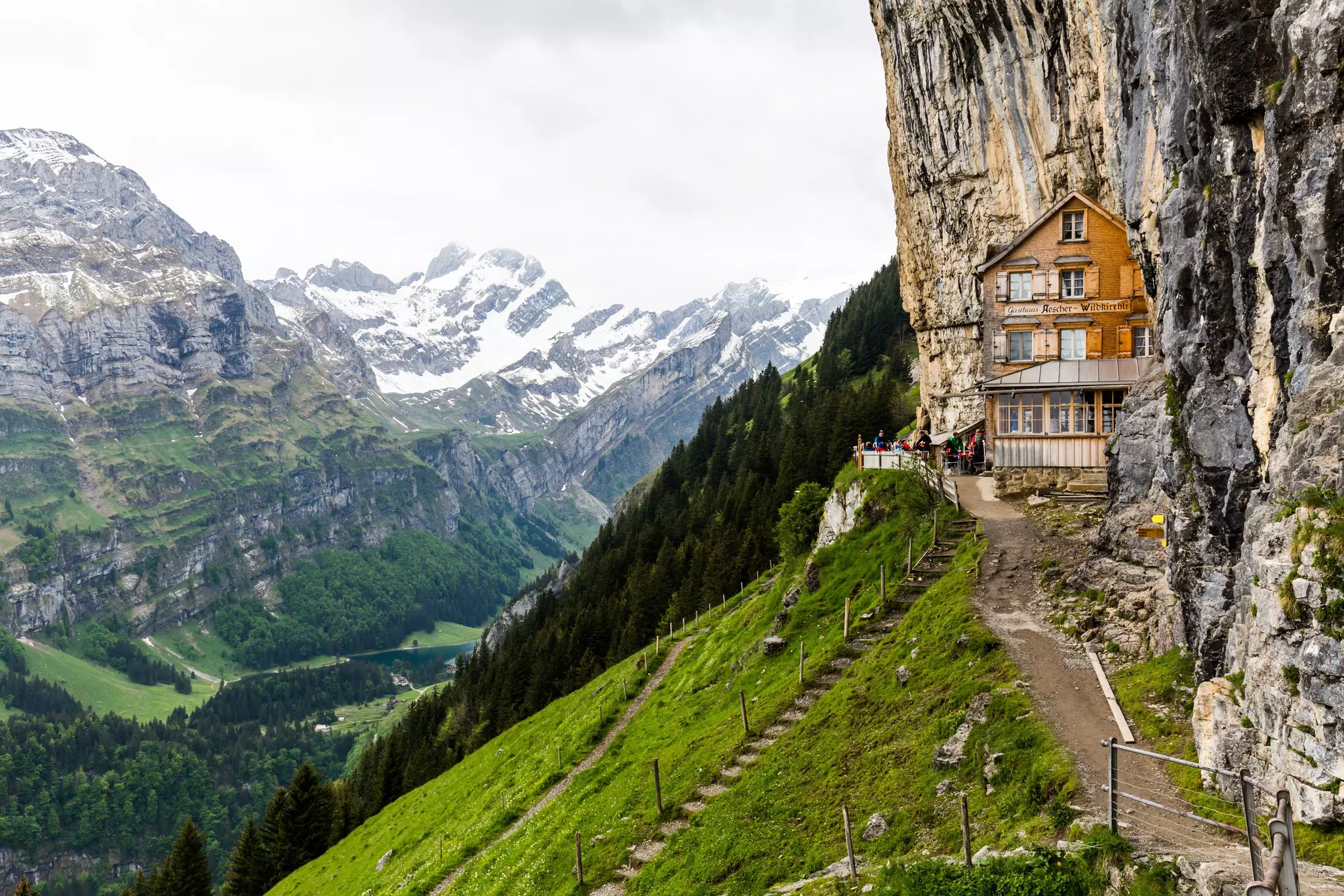 A Swiss-style chalet set back into the cliff face in a mountainous region.