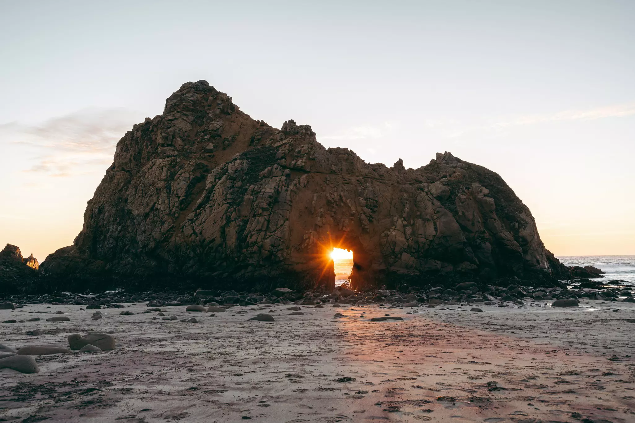 Sunset light passes through the arch of a rock formation, Pfeiffer Beach, Big Sur, California.