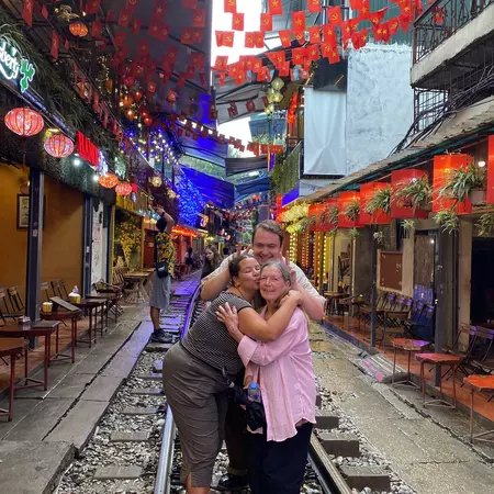 Two women and a man with their arms around each other, smiling while standing on a train track