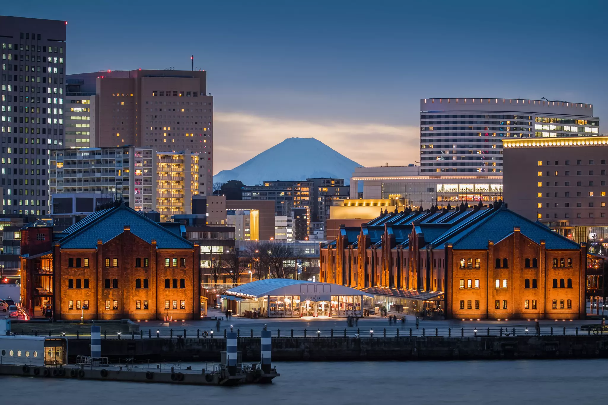 Red brick warehouses surrounded by skyscrapers with Mt. Fuji at dusk.