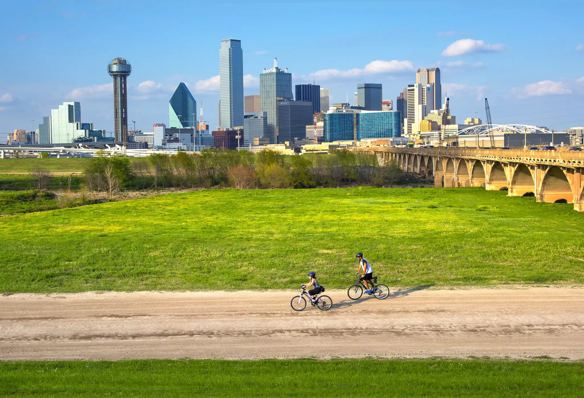Cyclists on the bike trail in Trinity River Park with a backdrop of the Dallas skyline.