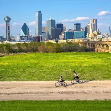 Cyclists on the bike trail in Trinity River Park with a backdrop of the Dallas skyline.