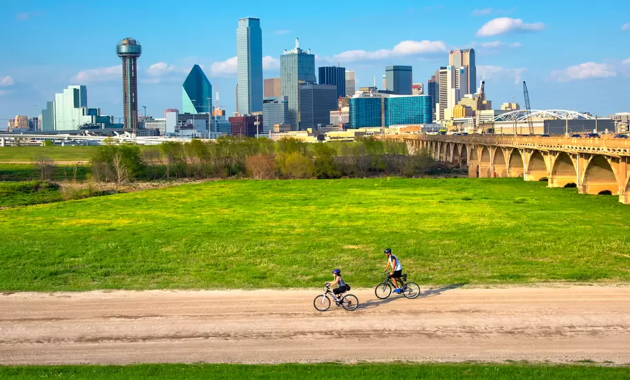 Cyclists on the bike trail in Trinity River Park with a backdrop of the Dallas skyline.