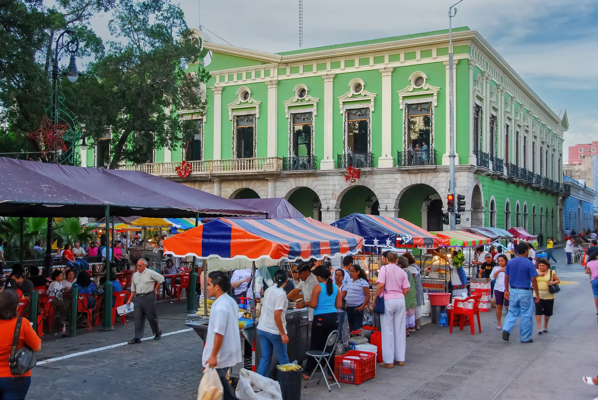 A view of a street market in a city center filled with stands and stalls. Historic, colorful buildings are visible in the background.