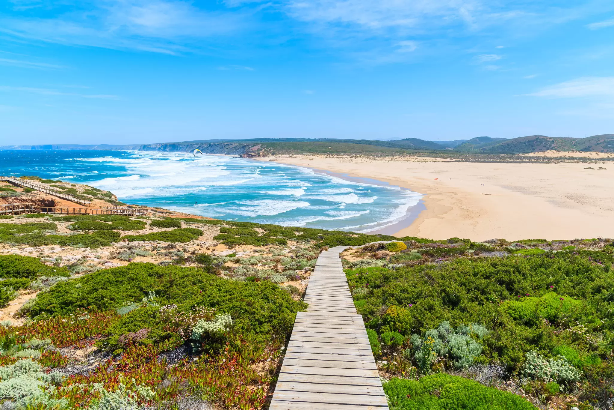 A wooden walkway leads down to a golden surf beach with waves crashing on its shores.
