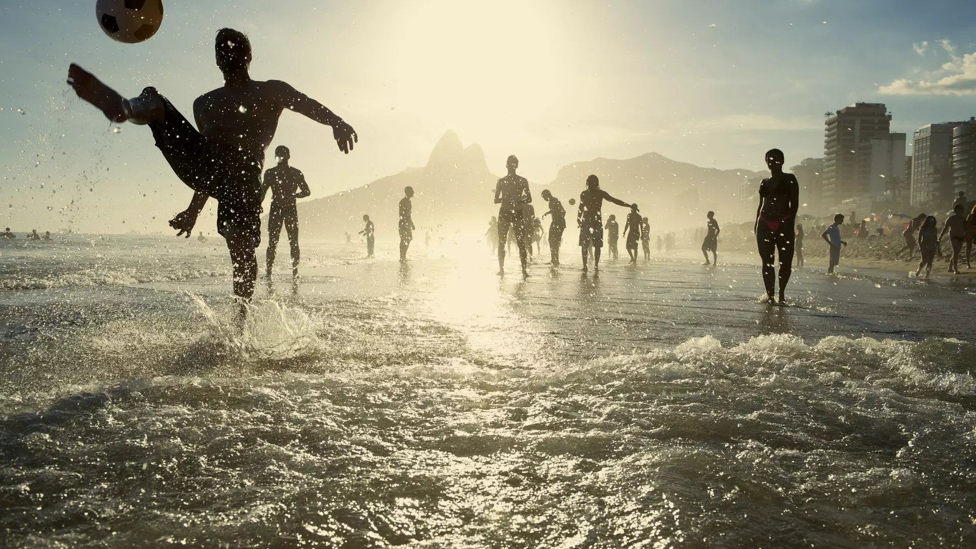 Carioca Brazilians playing altinho beach football in silhouettes kicking soccer balls in the waves of Ipanema Beach Rio de Janeiro Brazil