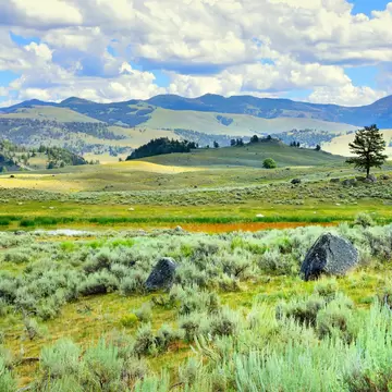 A green rolling landscape among larger mountains on a sunny day