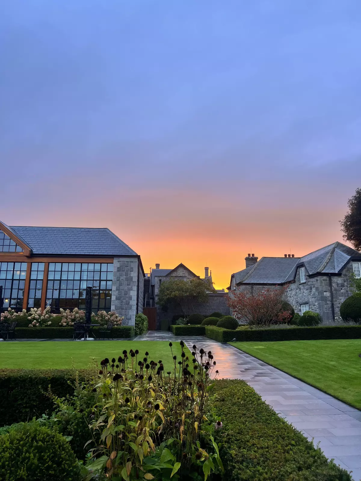 The sky glowing orange at sunset over some old stone cottages.