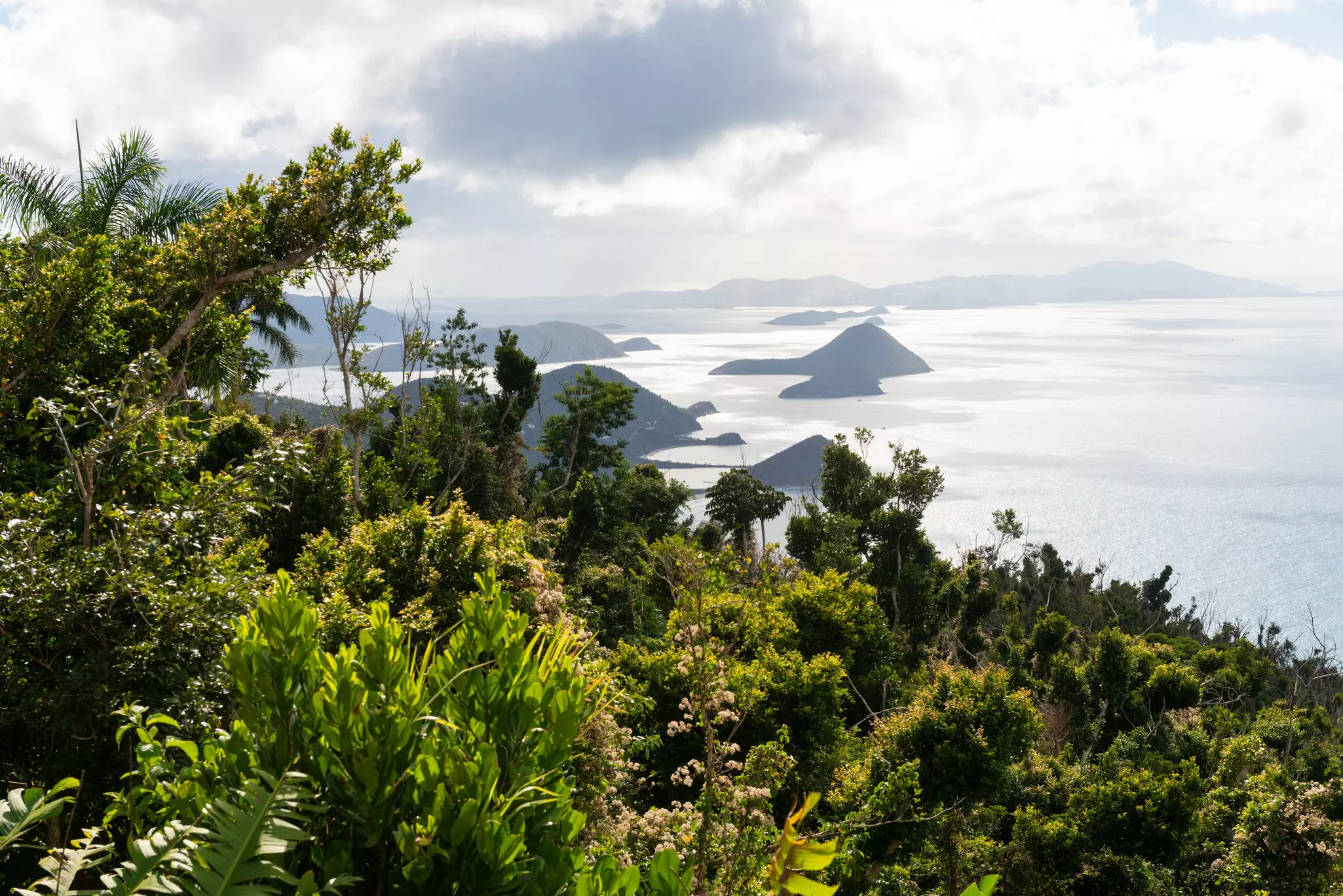 Islands are seen in the sea from the top of a lush hilltop on a tropical island.