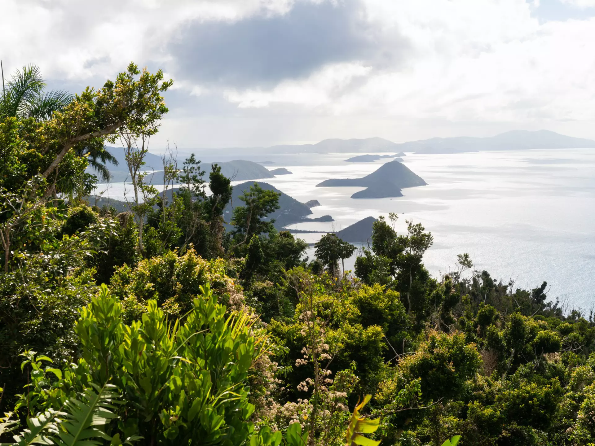Islands are seen in the sea from the top of a lush hilltop on a tropical island.