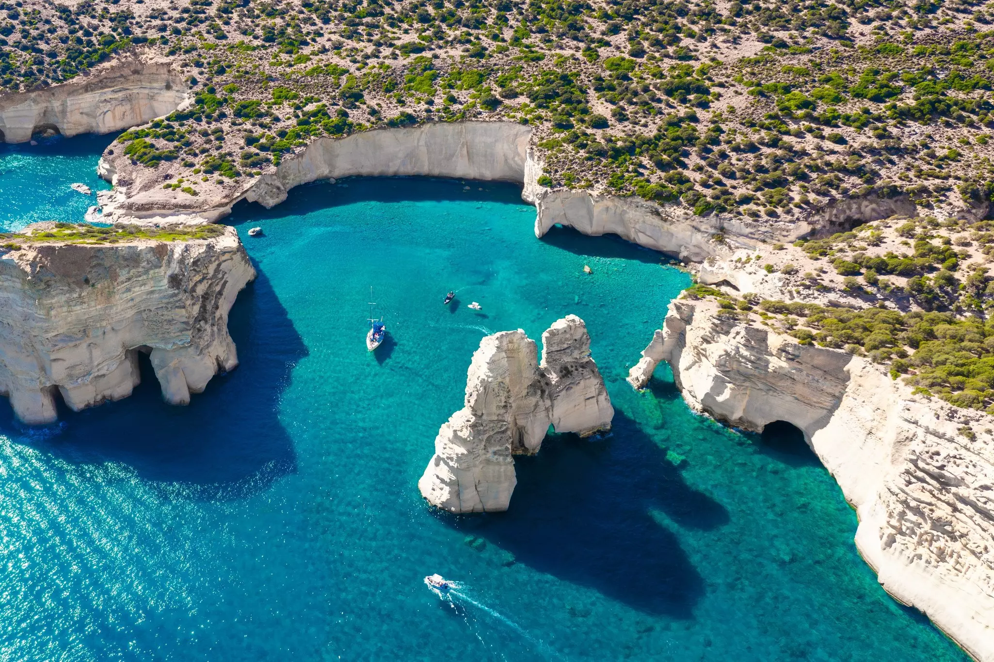 Boats in a turquoise cove, with white cliffs and large white rocks.