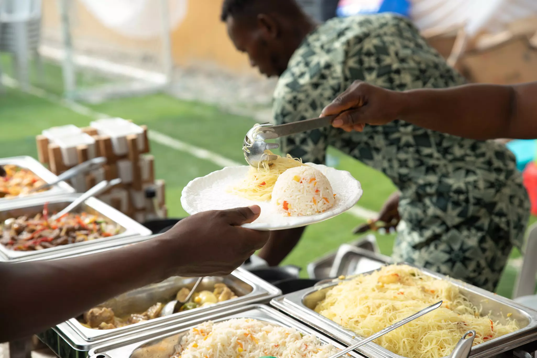 A person serves food on a white plate with a scoop of rice.