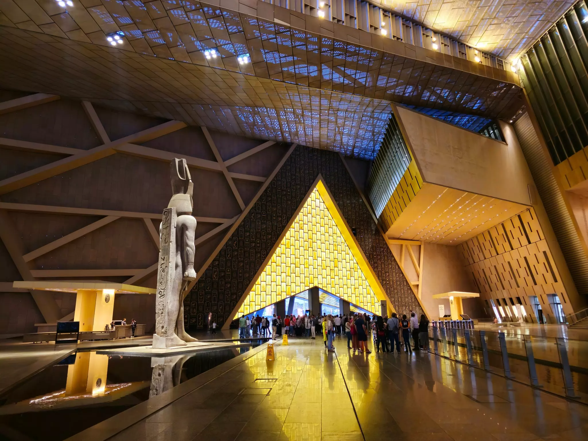 A museum hall with a large statue and an entrance with lighting shaped like a pyramid.