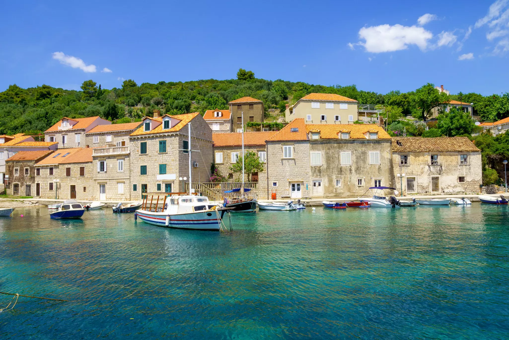 View of a fishing port on an island in Croatia. Blue water and sunny skies, boats floating in the water offshore. 