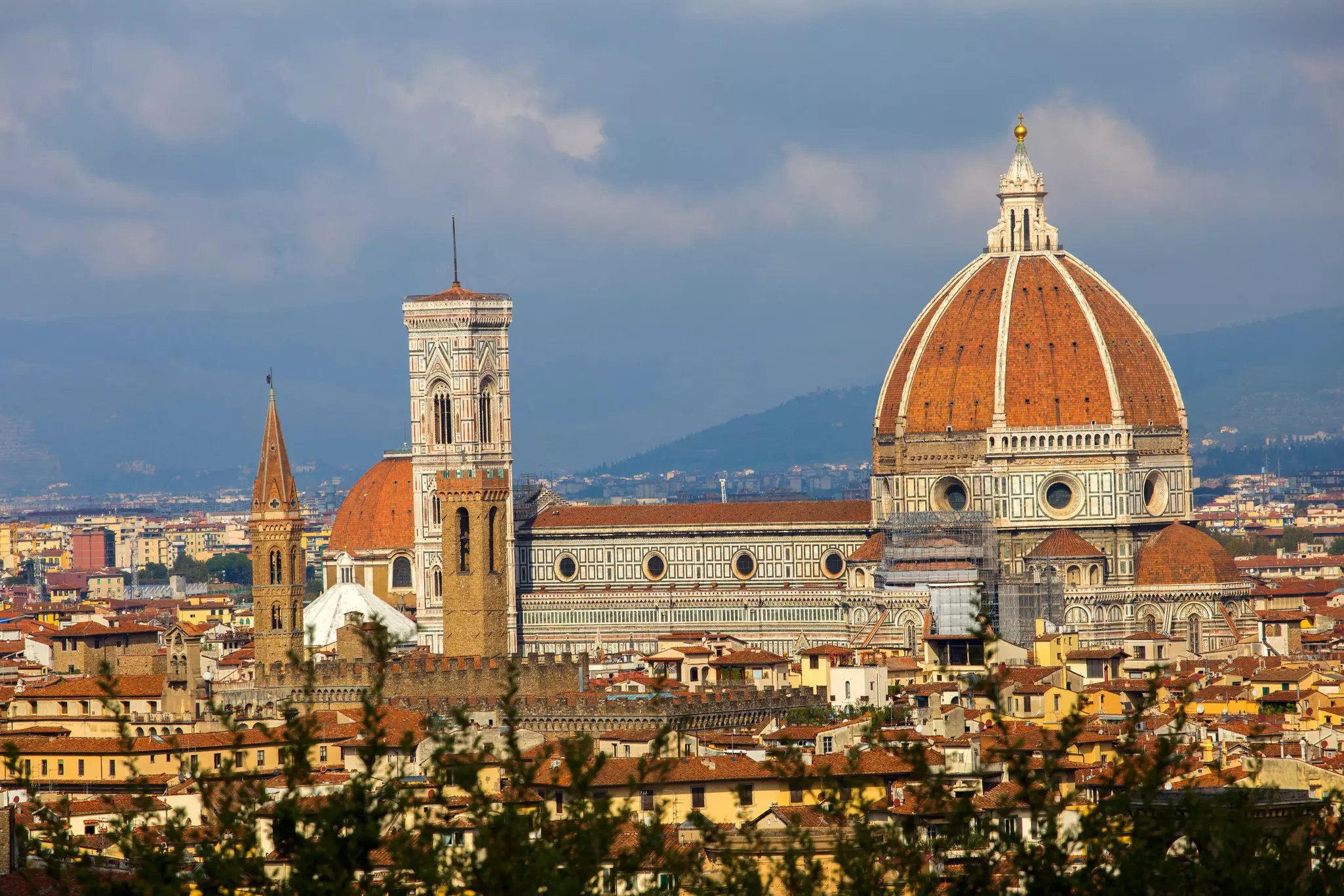 A large-domed cathedral rises above a city with clusters of red-roofed buildings
