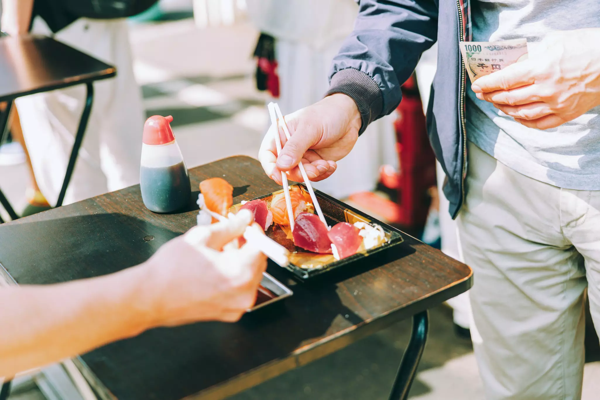 Two sets of hands holding chopsticks with sushi.