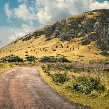 Dozens of moai statues dotting the grassy slope below Rano Raraku's cliffs, Easter Island, with a road in the foreground