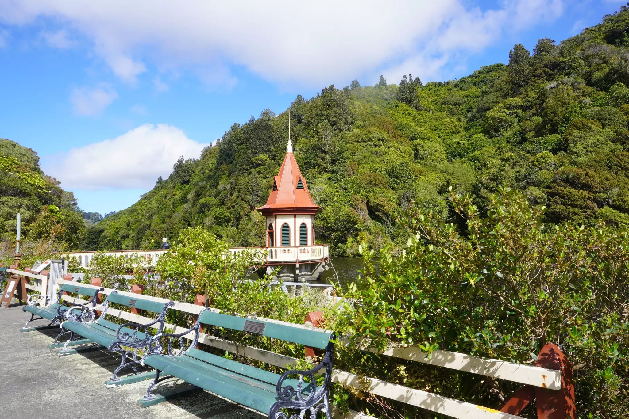 A small pier and tower with a conical red roof at the edge of a reservoir in an animal sanctuary surrounded with greenery.
