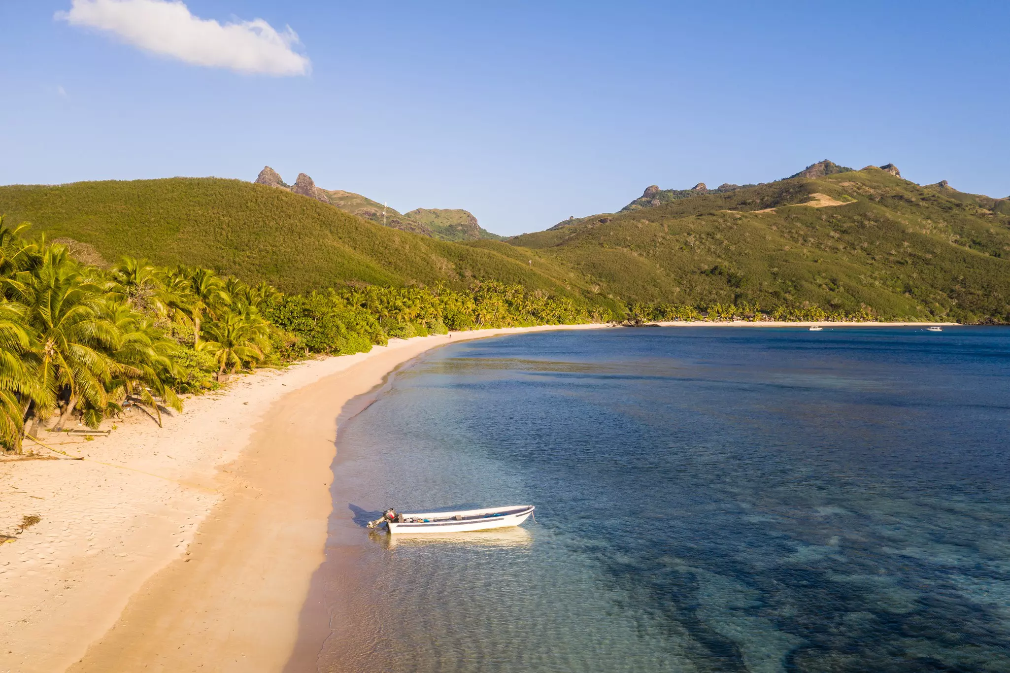 A small motorboat docked at the edge of a golden curve of sand backed by jungle.