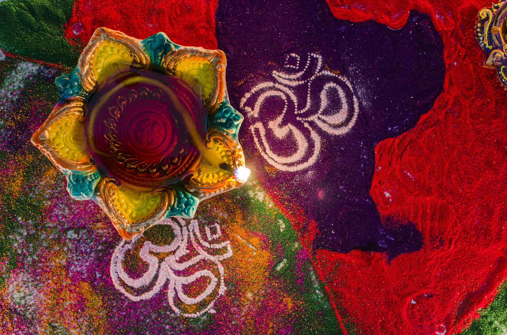 An overhead view of a coil of incense surrounded by colorful sand and flower petals forming patterns and written characters.