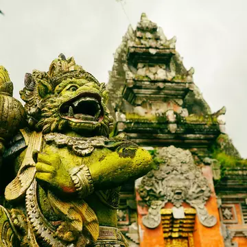 A stone figure with a green mossy covering; a temple is in the background.