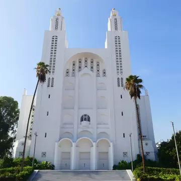 White art deco facade and twin towers of L'Eglise du Sacré Coeur in Casablanca under a blue sky, flanked by palms