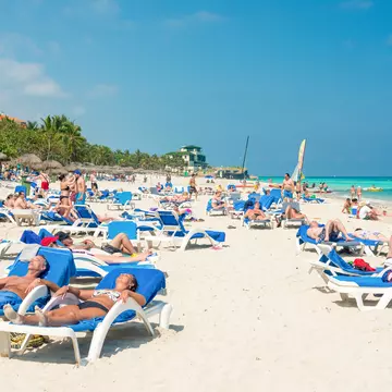People relax on chaise lounges in the sun on a tropical beach.