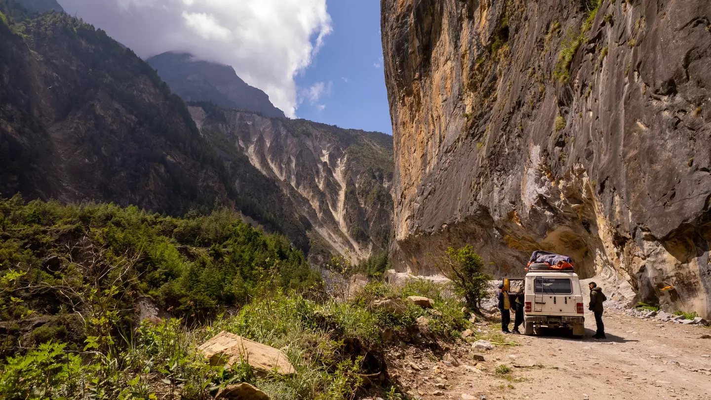 People stopping by their off-road vehicle during a drive through a mountain pass on a sunny day.
