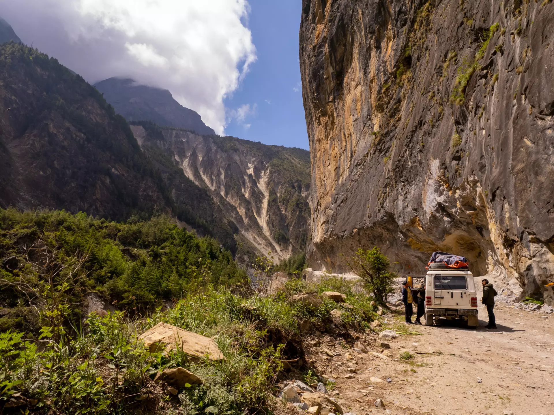 People stopping by their off-road vehicle during a drive through a mountain pass on a sunny day.