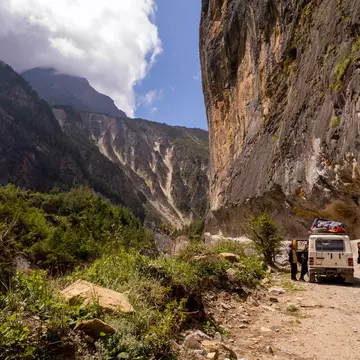 People stopping by their off-road vehicle during a drive through a mountain pass on a sunny day.