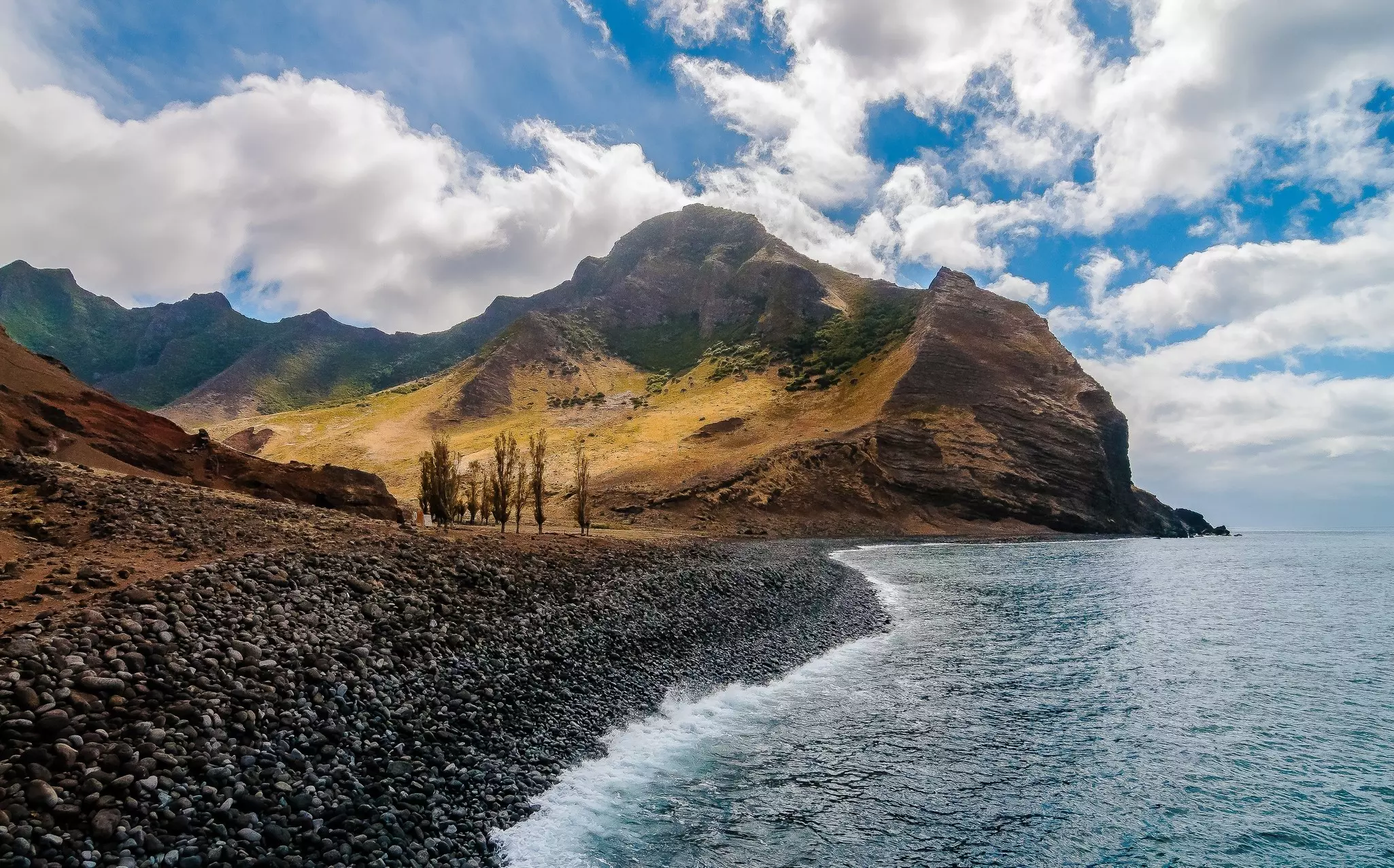 An empty rocky shoreline wiht a large craggy mountain peak rising in the distance