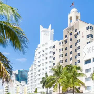 A row of art-deco hotels on a busy street lined with palm trees.