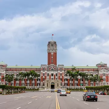 Taipei's Red and white Presidential Office Building designed in a neo-baroque style at the end of a wide street with traffic on it.