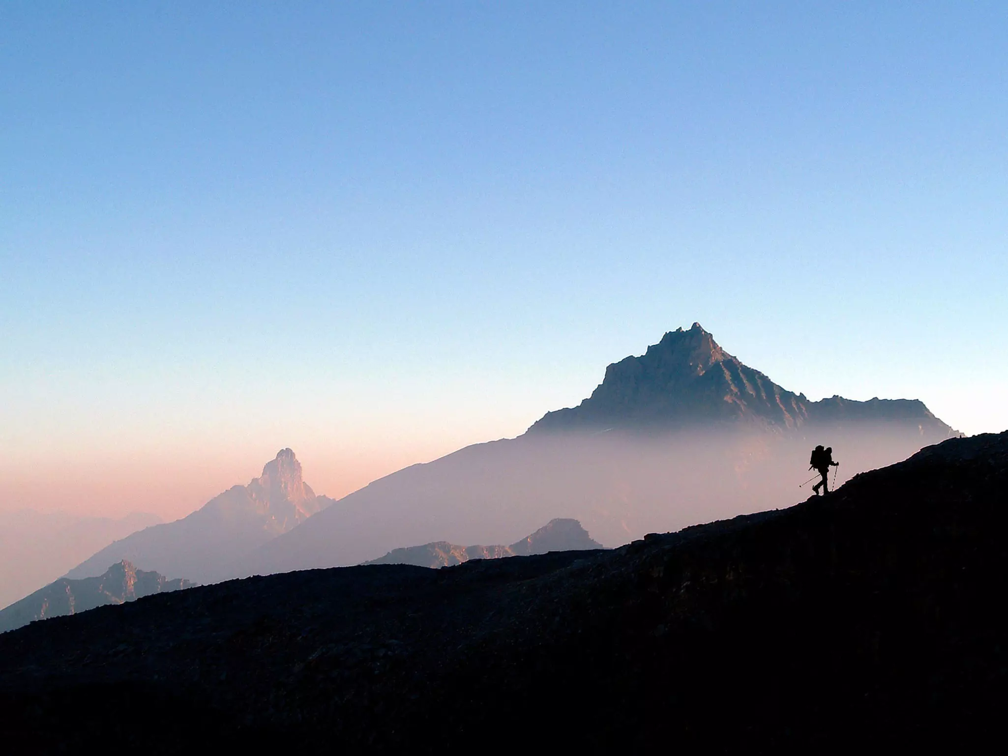 Silhouette of a hiker with a backpack climbing a ridge in the mountains of Gran Paradiso National Park