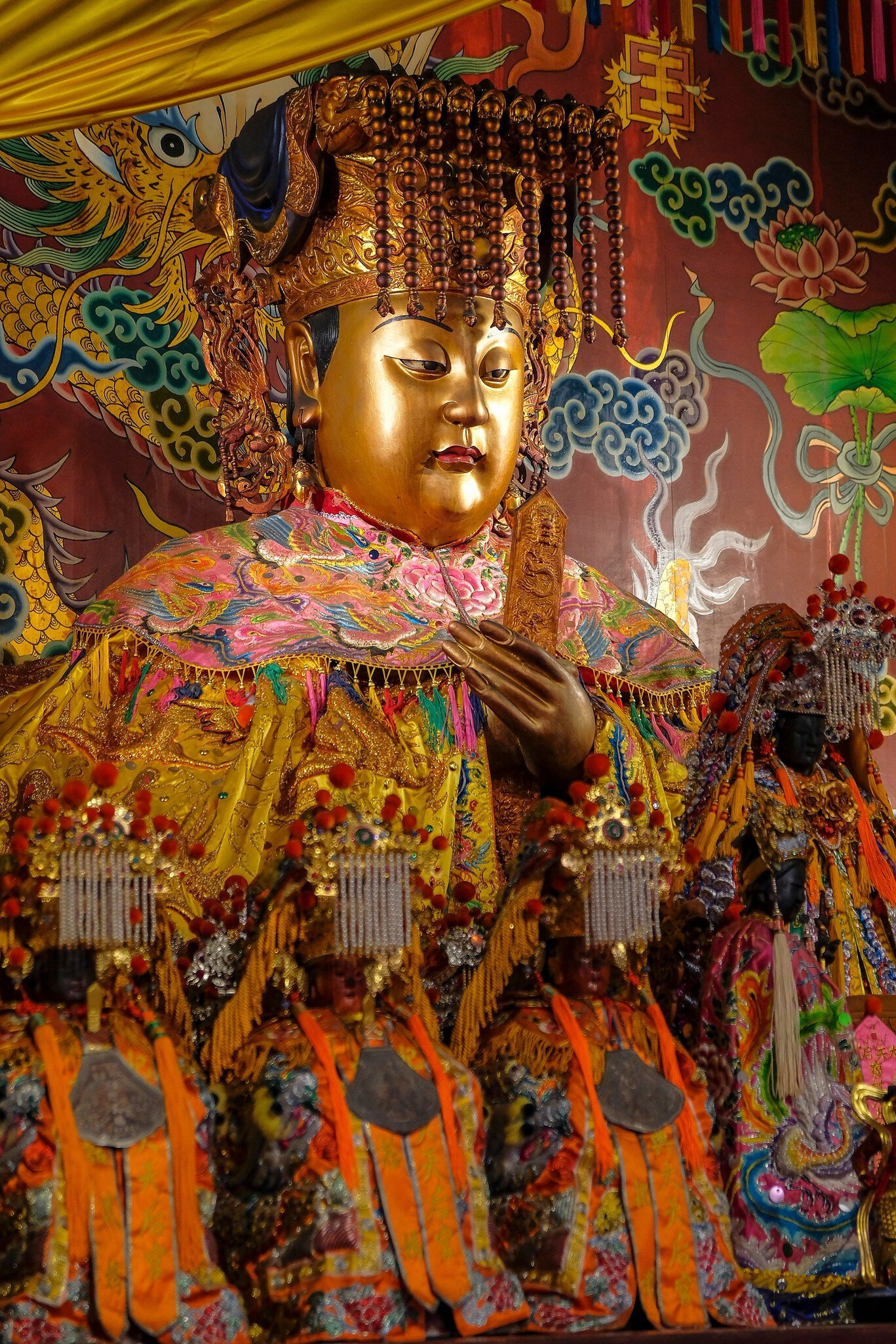 A gold-faced deity figure in a beaded crown and pink embroidered cape, with rows of smaller figures below