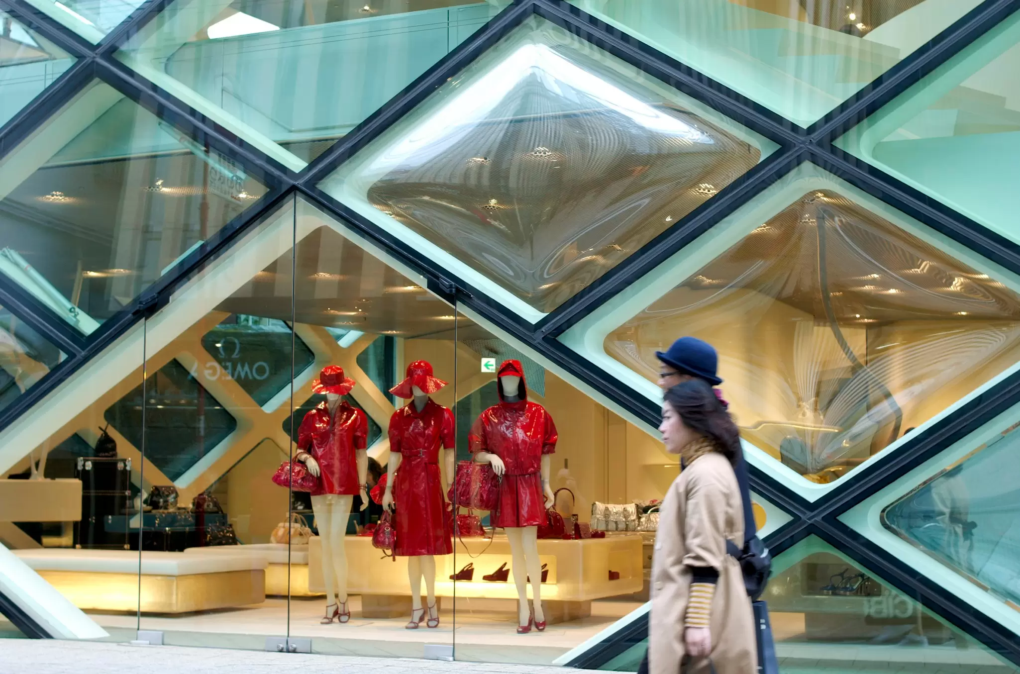 People walk by a store in Aoyama with mannequins in red on display through its diamond-shaped windows