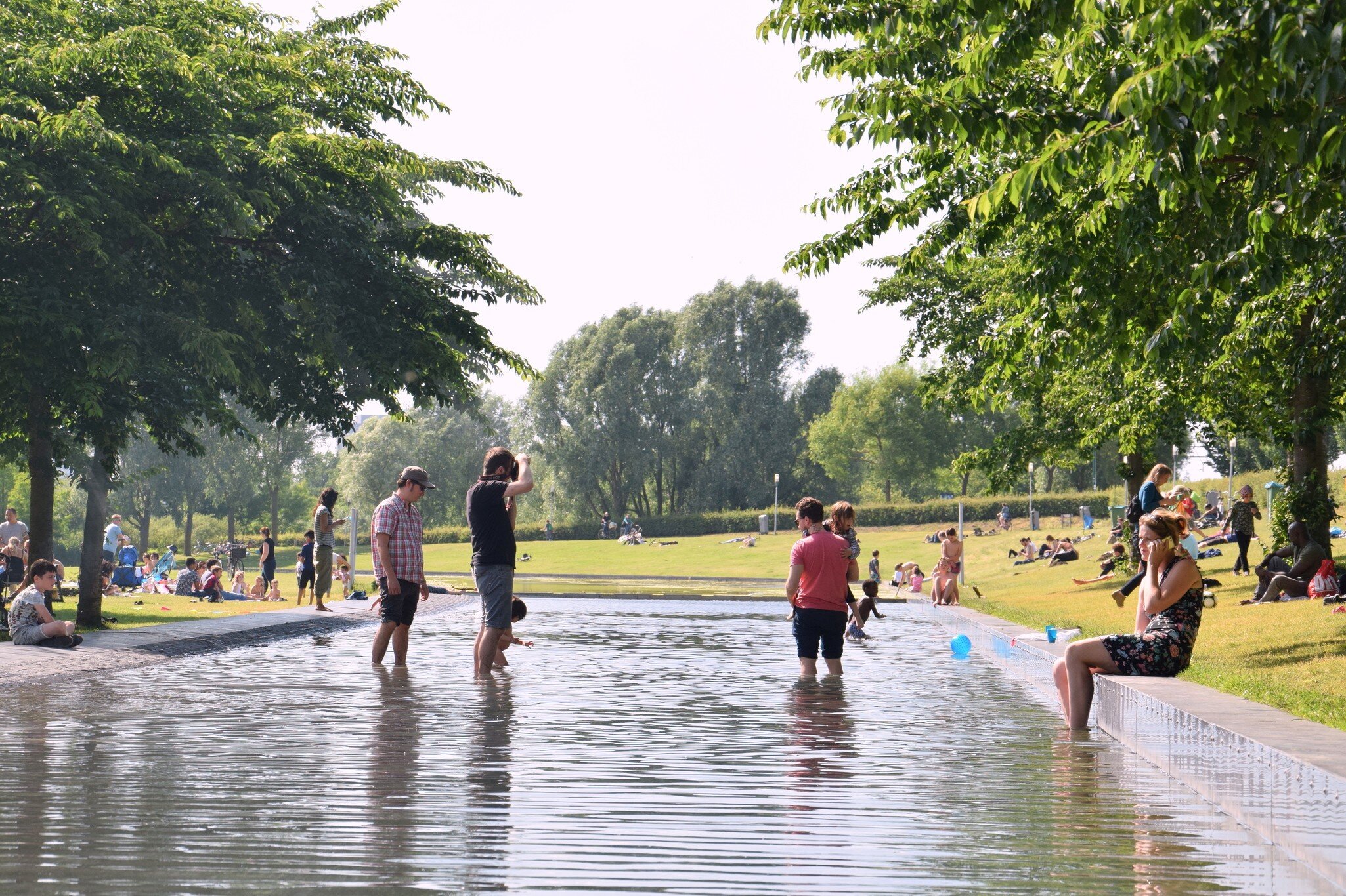 Families with children enjoy the sunny day bathing in a swimming pool in Westerpark, Amsterdam, surrounded by greenery.