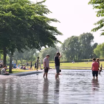 Families with children enjoy the sunny day bathing in a swimming pool in Westerpark, Amsterdam, surrounded by greenery.